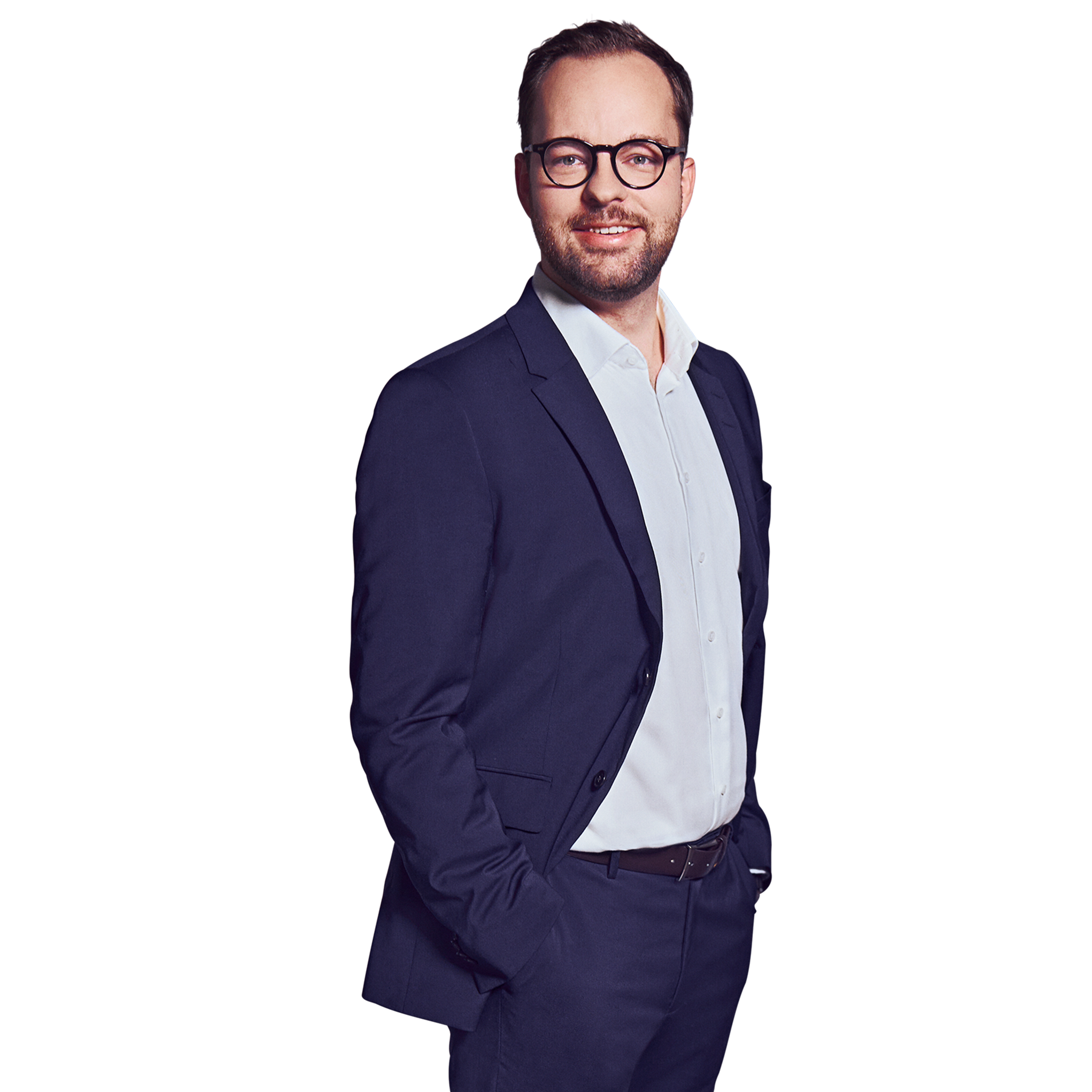Männliche Person, braune kurze Haare, dunkelblaue Augen mit Brille, lächelnd mit Bart, trägt ein weißes Hemd und einen dunkelblauen Anzug, stehend mit beiden Händen in den Hosentaschen