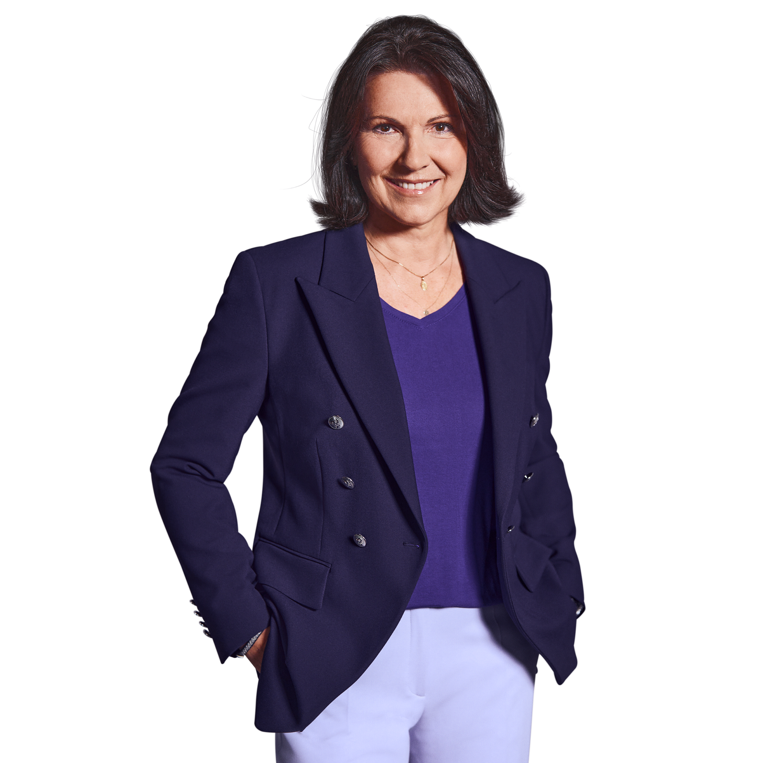 Portrait photo of Constanze Schöffmann, Director of HR at Kemény Boehme Consultants (KBC). A woman with shoulder-length, dark brown hair streaked with gray, looks into the camera with a friendly smile. She is wearing a dark blue double-breasted blazer over a purple V-neck shirt and white pants, as well as a delicate gold necklace. Her hands are in her pockets, and she has a confident and welcoming demeanor.