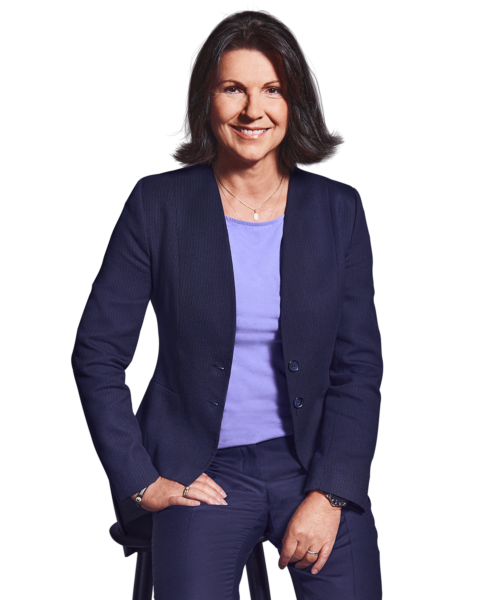 Porträtfoto von Constanze Schöffmann, Director HR bei Kemény Boehme Consultants (KBC). Frau mit schulterlangem, dunkelbraunem Haar blickt freundlich lächelnd in die Kamera. Trägt ein dunkelblaues Doppelreiher-Sakko mit goldenen Knöpfen über einem lila V-Ausschnitt-Top sowie eine dunkelblaue Hose und eine zarte goldene Halskette, eine Hand lässig in der Hosentasche, leicht an einen Stuhl gelehnt.