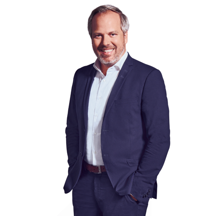 Portraitbild von Georg Huber, Senior Partner bei Kemény Boehme Consultants, der lächelnd mit beiden Händen in den Hosentaschen in die Kamera blickt