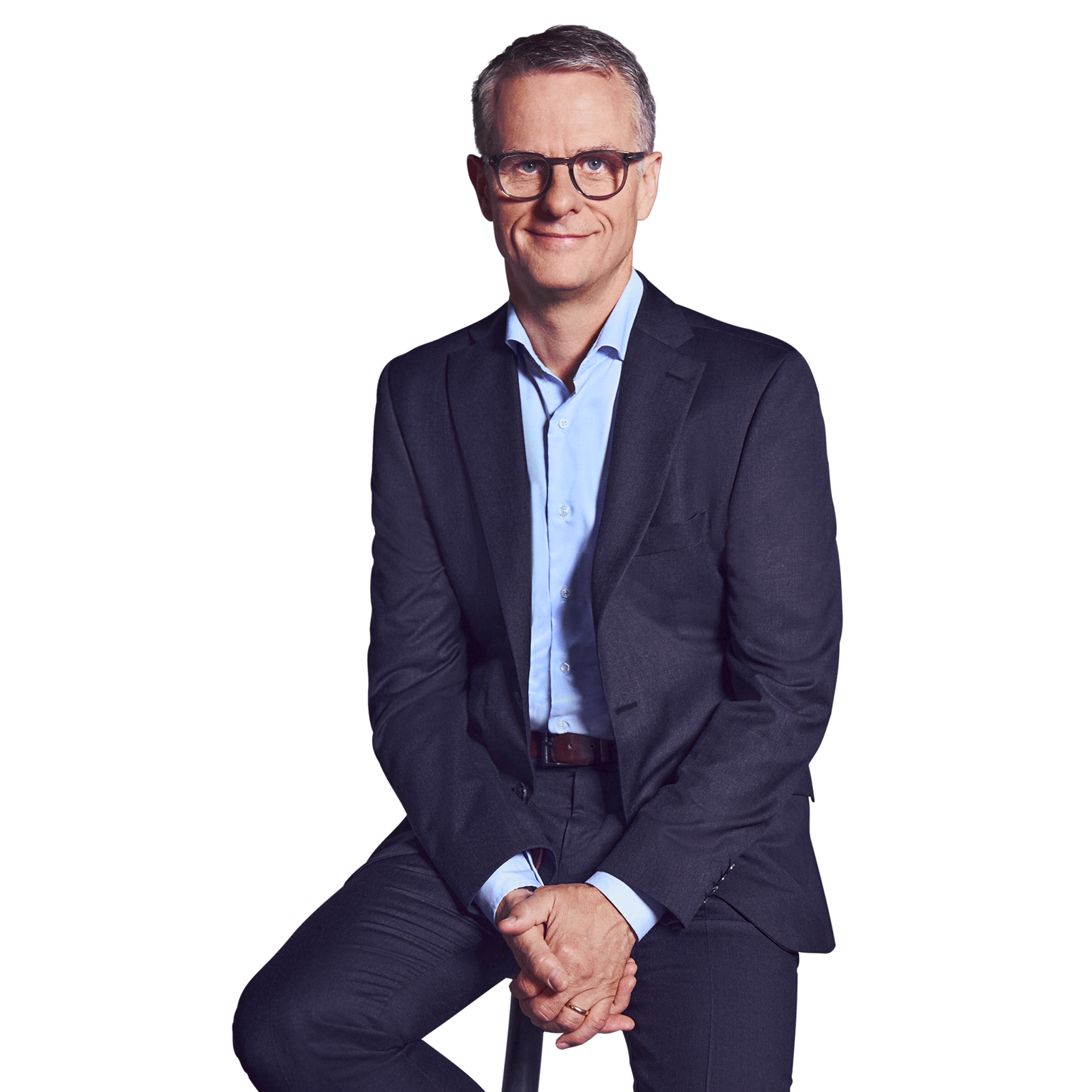 Porträtfoto von John Dowling, Partner bei Kemény Boehme Consultants (KBC). Mann mit kurzen, grau-melierten Haaren und markanter dunkelbrauner Rechteckbrille blickt ruhig und konzentriert in die Kamera. Trägt einen dunkelblauen Anzug mit passendem Sakko und Hose über einem hellblauen Hemd ohne Krawatte, eine Hand lässig in der Hosentasche, die andere locker seitlich am Körper, aufrechte und souveräne Haltung.