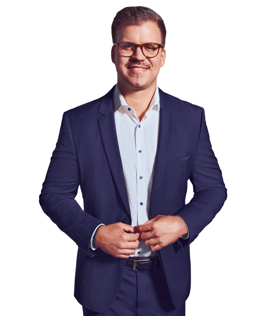 Porträtfoto von Markus Stingl, Manager bei Kemény Boehme Consultants (KBC). Mann mit kurzen, dunkelbraunen Haaren, einem gepflegten Kinnbärtchen und einer markanten braungemusterten Hornbrille blickt freundlich lächelnd in die Kamera. Trägt einen dunkelblauen Anzug mit passendem Sakko und Hose über einem weißen Hemd mit blauen Knöpfen ohne Krawatte sowie einen schwarzen Ledergürtel, beide Hände locker vor dem Körper verschränkt, offene und sympathische Haltung.