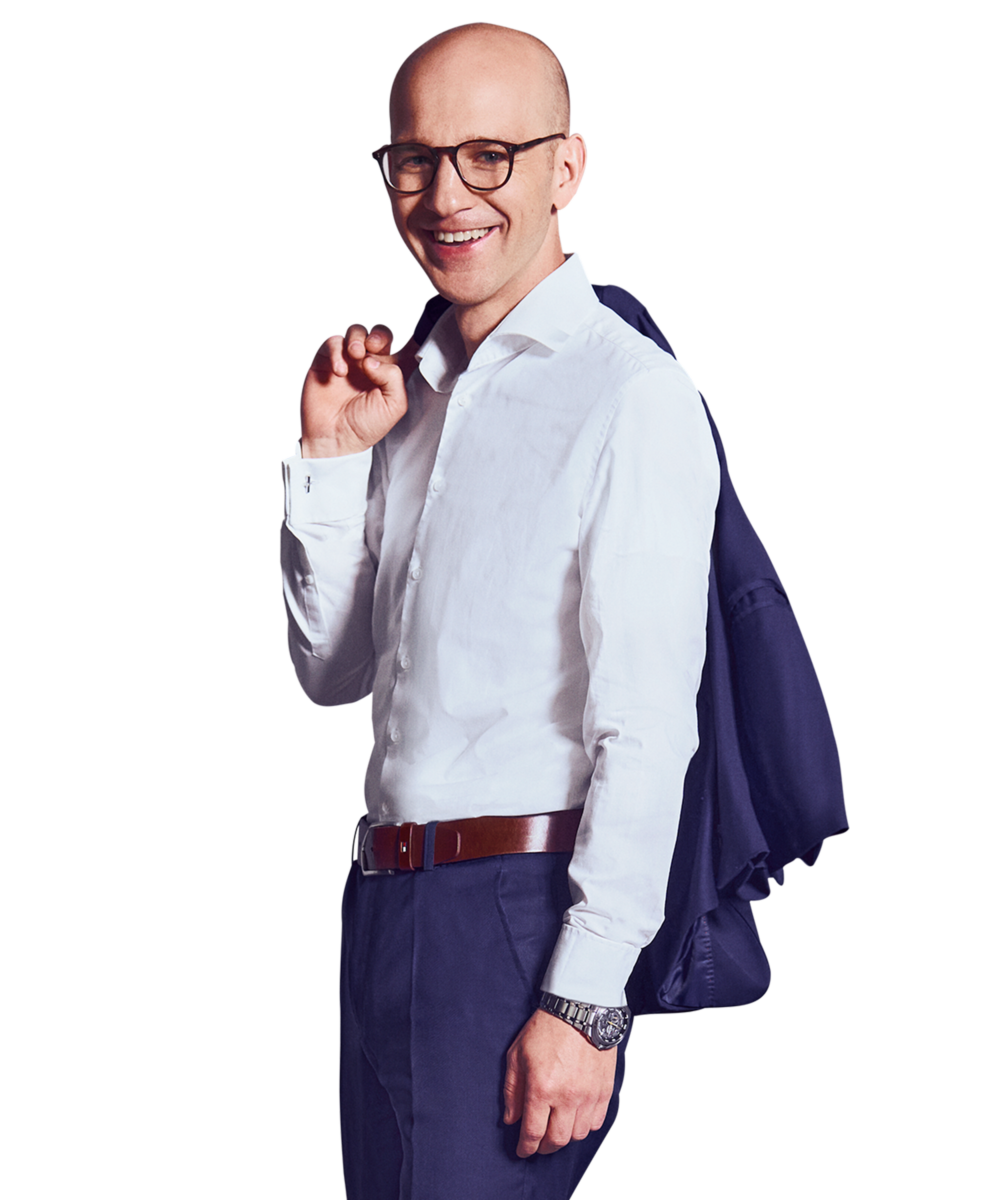 Porträtfoto von Martin Betz, Director bei Kemény Boehme Consultants (KBC). Mann mit rasiertem Kopf und markanter dunkler Rechteckbrille, blickt freundlich lächelnd in die Kamera. Trägt einen dunkelblauen Anzug mit passendem Sakko über der Schulter und Hose über einem hellblauen Hemd ohne Krawatte, einen cognacfarbenen Ledergürtel sowie eine silberne Armbanduhr am rechten Handgelenk, aufrechte und selbstbewusste Haltung.