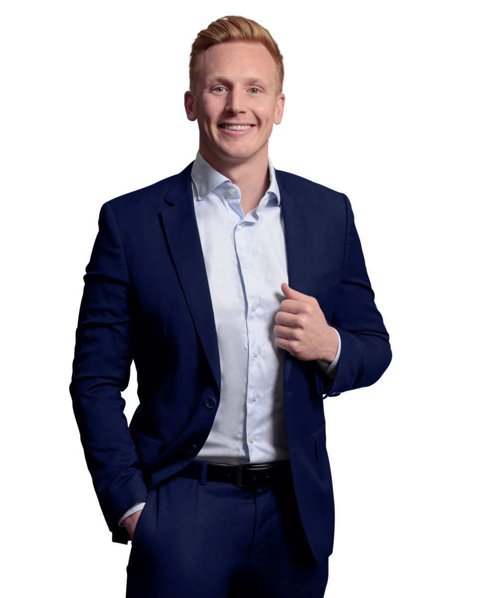 Porträtfoto von Nils Lauer-Neff, Manager bei Kemény Boehme Consultants (KBC). Mann mit hellblonden Haaren blickt freundlich lächelnd in die Kamera. Trägt einen dunkelblauen Anzug mit passendem Sakko und Hose über einem weißen Hemd ohne Krawatte sowie einen schwarzen Ledergürtel, eine Hand in der Hosentasche und eine am Revere, offene und sympathische Haltung.