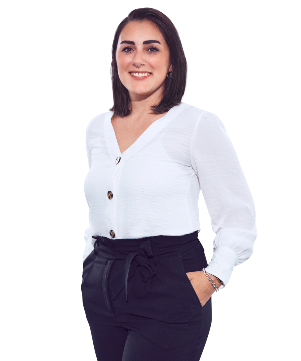 Porträtfoto von Serap Aydin, Office Manager HR bei Kemény Boehme Consultants (KBC). Frau mit schulterlangem, glattem, dunkelbraunem Haar blickt breit lächelnd in die Kamera. Trägt eine elegante weiße Bluse mit V-Ausschnitt und goldenen Knöpfen sowie eine schwarze Hose mit Bindegürtel in der Taille und ein silbernes Kettenarmband, eine Hand locker in der Hosentasche, leichte Drehung zur Seite, offene und freundliche Haltung.