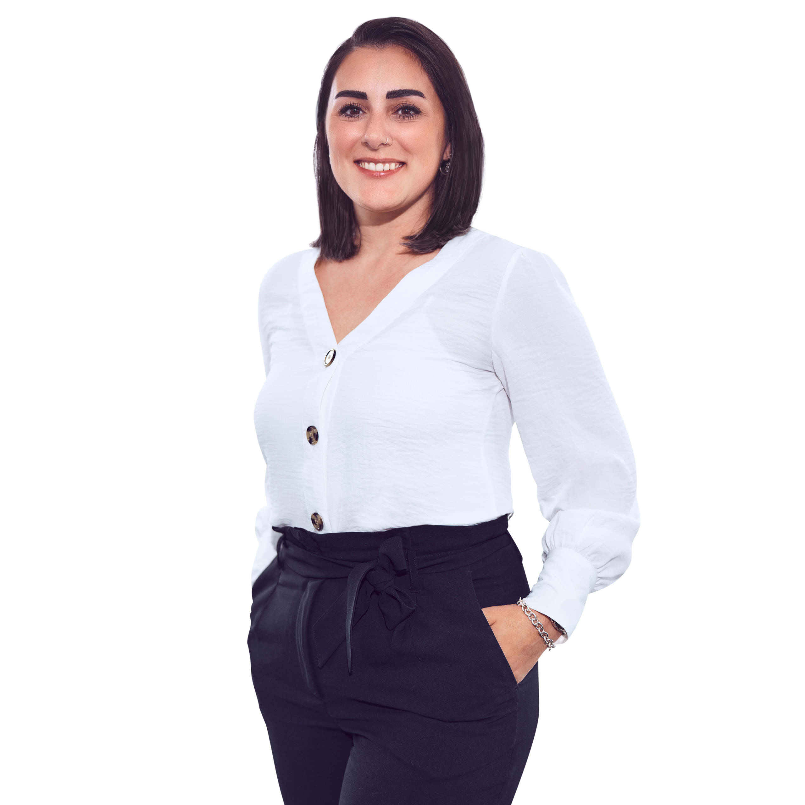 Porträtfoto von Serap Aydin, Office Manager HR bei Kemény Boehme Consultants (KBC). Frau mit schulterlangem, glattem, dunkelbraunem Haar blickt breit lächelnd in die Kamera. Trägt eine elegante weiße Bluse mit V-Ausschnitt und goldenen Knöpfen sowie eine schwarze Hose mit Bindegürtel in der Taille und ein silbernes Kettenarmband, eine Hand locker in der Hosentasche, leichte Drehung zur Seite, offene und freundliche Haltung.