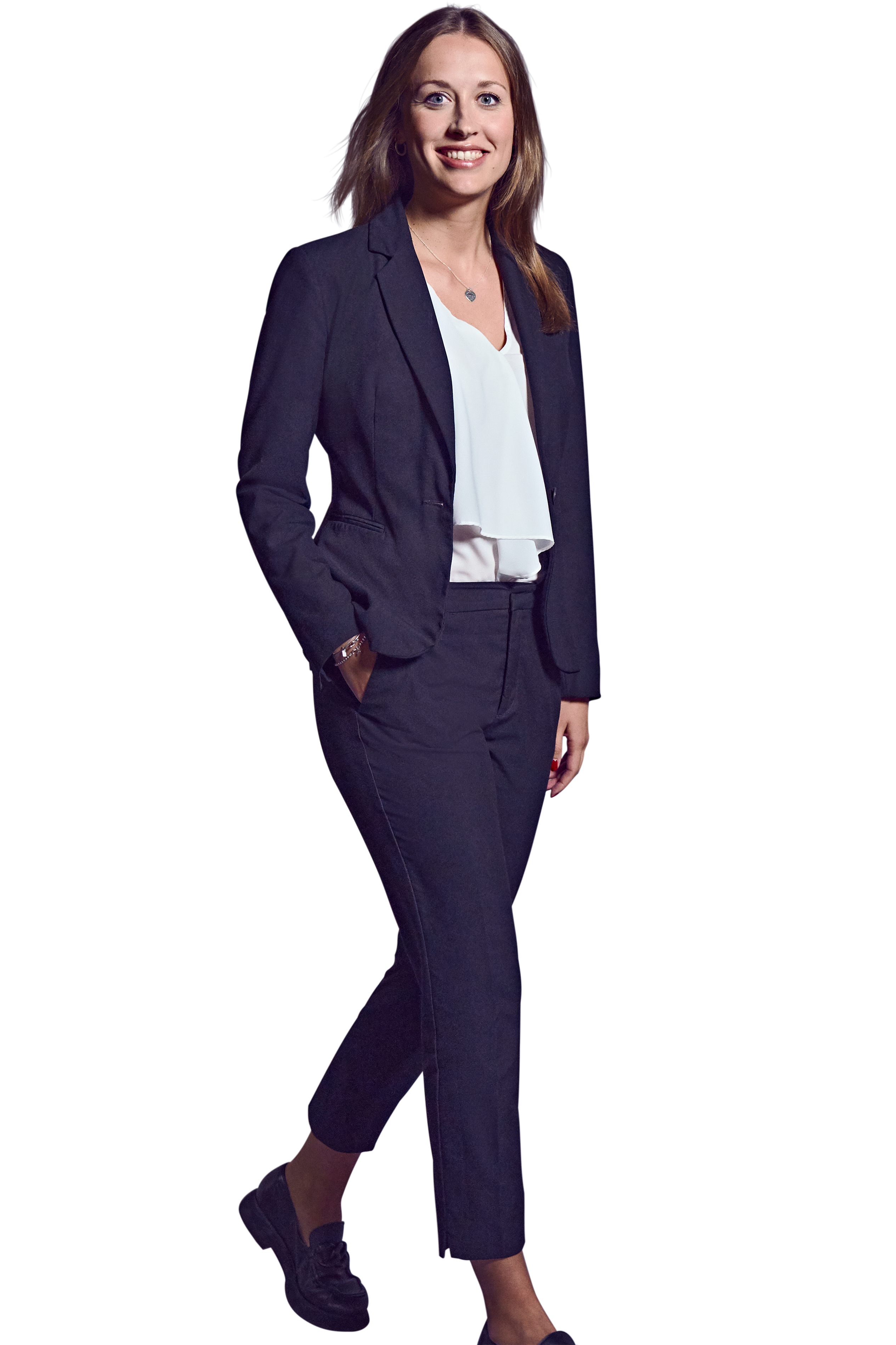 Weibliche Person, braune mittellange Haare, grüne Augen, lächelnd, trägt ein weißes Oberteil, dunkelblaue Hose und Blazer, gehend mit der rechten Hand in der Hosentasche