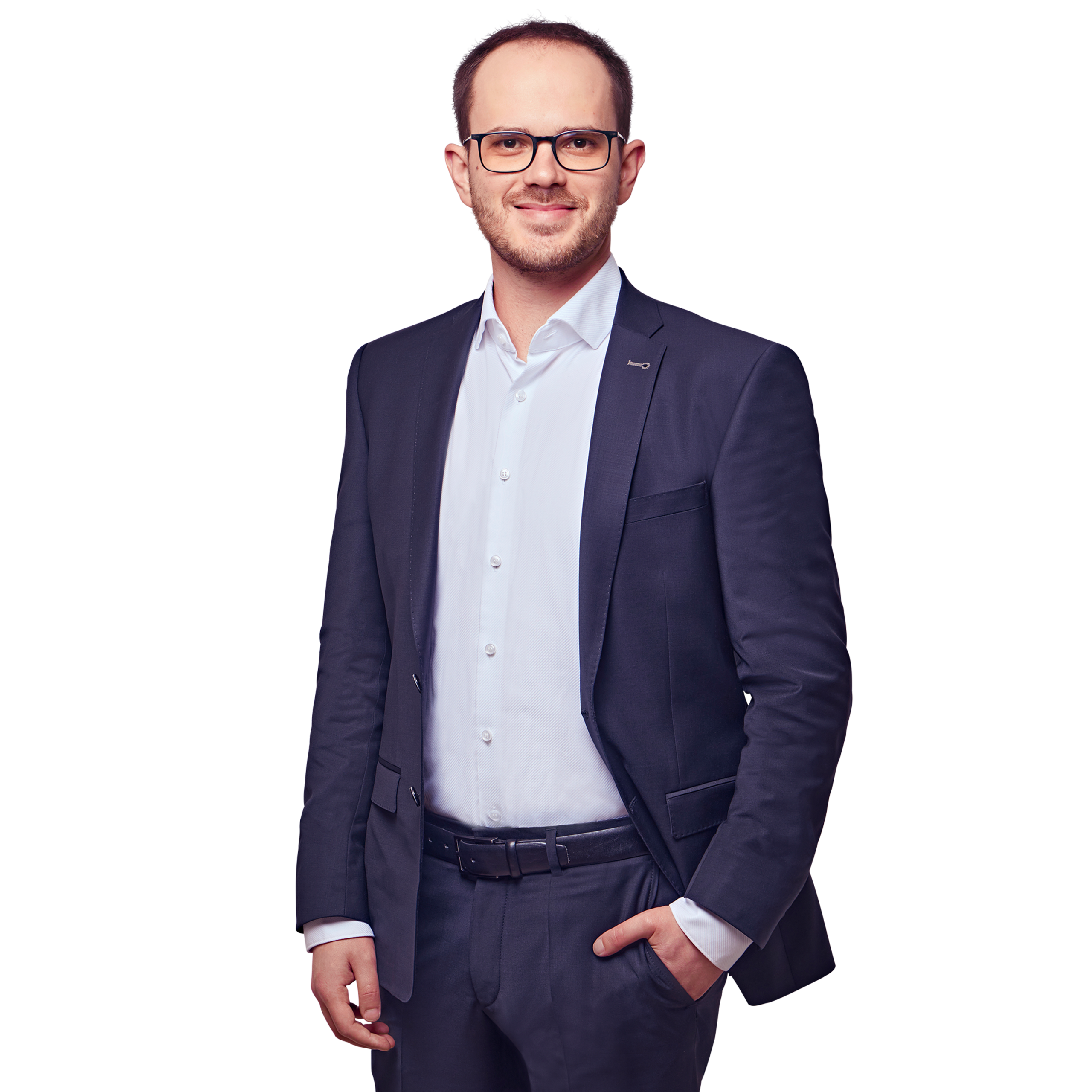 Porträtfoto von Gregor Kühn, Senior Consultant bei Kemény Boehme Consultants (KBC). Mann mit kurzem, dunkelbraunem Haar und gepflegtem Kurzbart trägt eine markante dunkle Rechteckbrille und blickt freundlich lächelnd in die Kamera. Trägt einen dunklen Blazer mit kleinem Anstecker am Revers über einem hellblauen Hemd ohne Krawatte sowie einen dunklen Gürtel, eine Hand locker in der Hosentasche, aufrechte und sympathische Haltung.