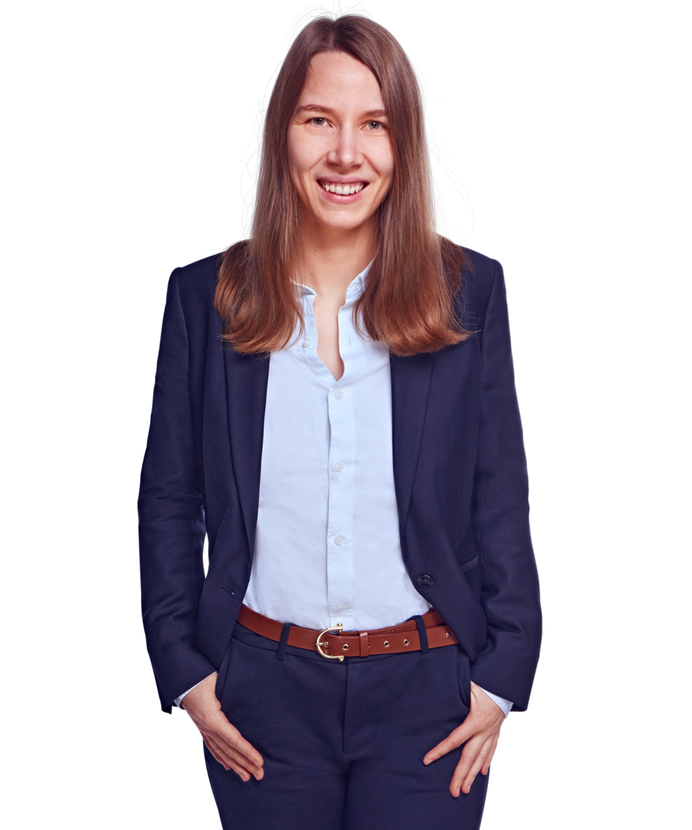 Porträtfoto von Luisa Ehmcke, Senior Consultant bei Kemény Boehme Consultants (KBC). Frau mit langem, glattem, dunkelbraunem Haar blickt breit lächelnd in die Kamera. Trägt einen dunklen Blazer über einer hellblauen, offen getragenen Bluse sowie eine markante cognacfarbene Ledergürtel mit goldener Schnalle und dunkle Hose, beide Hände locker in den Hosentaschen, aufrechte und offene Haltung.