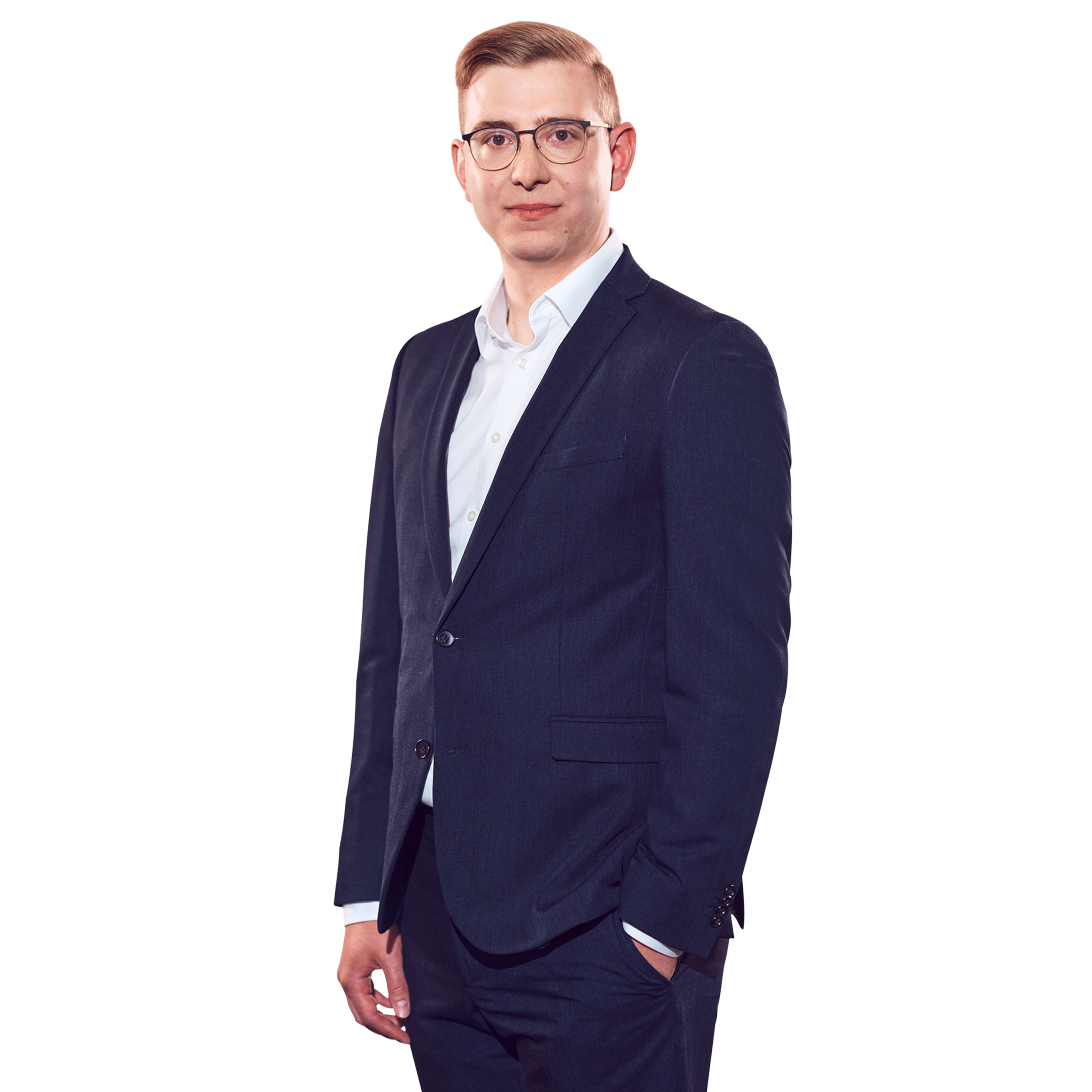 Porträtfoto von Florian Fuchs, Manager bei Kemény Boehme Consultants (KBC). Mann mit kurzem, hellblondem bis rötlichem Haar und einer markanten dunklen Rundbrille blickt ruhig und konzentriert in die Kamera. Trägt einen dunklen Zweiknopf-Blazer über einem hellblauen Hemd ohne Krawatte, eine Hand locker in der Hosentasche, die andere seitlich am Körper, leicht zur Seite gedrehte, sachliche und professionelle Haltung.