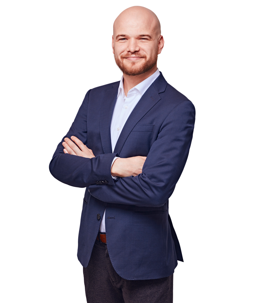Porträtfoto von Fritz Anzinger, Senior Consultant bei Kemény Boehme Consultants (KBC). Mann mit rasiertem Kopf und gepflegtem rotblondem Vollbart blickt freundlich lächelnd in die Kamera. Trägt einen dunkelblauen Zweiknopf-Blazer über einem hellblauen Hemd ohne Krawatte sowie einen cognacfarbenen Gürtel, Arme selbstbewusst vor der Brust verschränkt, leicht zur Seite gedrehte, offene und charismatische Haltung.
