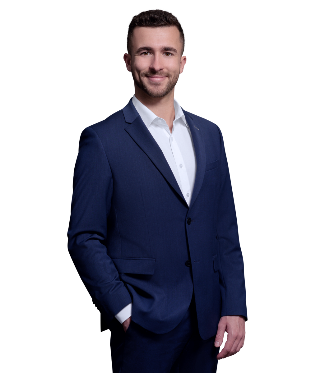 Porträtfoto von Tobias Wütherich, Senior Consultant bei Kemény Boehme Consultants (KBC). Mann mit kurzen dunkelbraunen Haaren und leichtem Bartschatten, blickt freundlich lächelnd in die Kamera. Trägt ein royalblaues Sakko über einem weißen Hemd ohne Krawatte, entspannte Haltung mit einer Hand in der Hosentasche.
