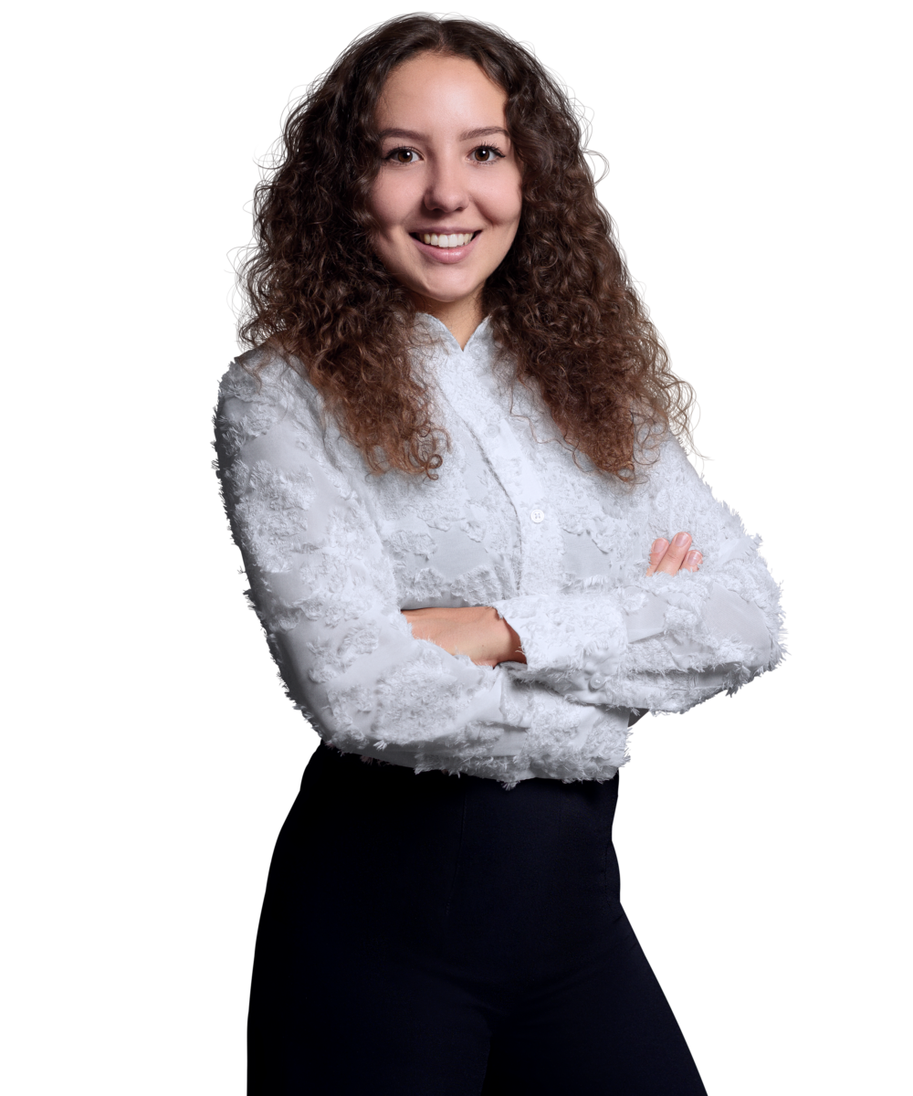 Porträtfoto von Lara-Marie Michalek, Junior Consultant bei Kemény Boehme Consultants (KBC). Frau mit langen, lockigen dunkelbraunen Haaren, blickt freundlich lächelnd in die Kamera. Trägt eine weiße Bluse mit floralem Strukturmuster und eine schwarze Hose, Arme verschränkt, selbstbewusste und offene Haltung.