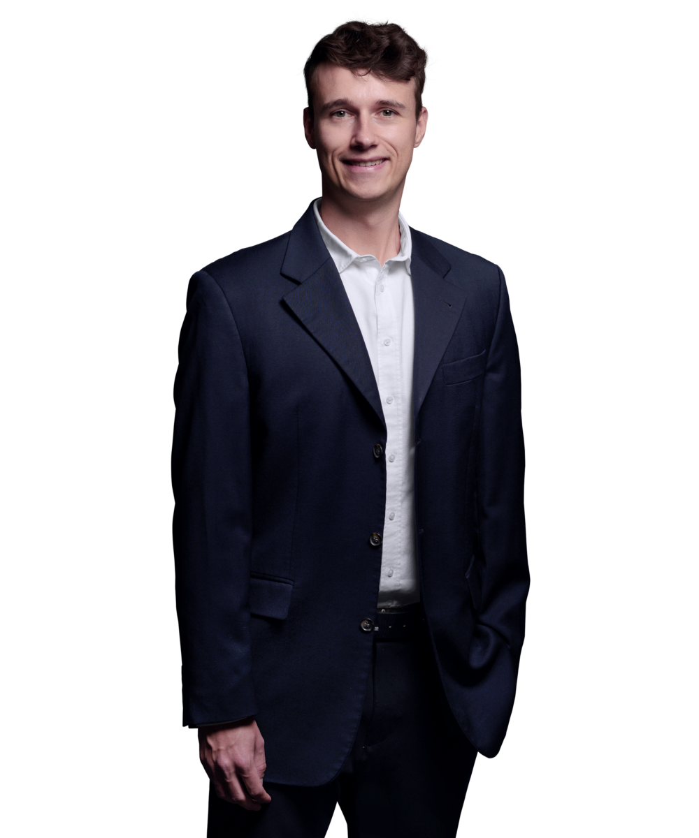 Porträtfoto von Julian Otto, Consultant bei Kemény Boehme Consultants (KBC). Mann mit lockigen dunkelbraunen Haaren, blickt freundlich lächelnd in die Kamera. Trägt ein dunkelblaues Sakko über einem weißen Hemd ohne Krawatte, entspannte Haltung mit einer Hand in der Hosentasche.