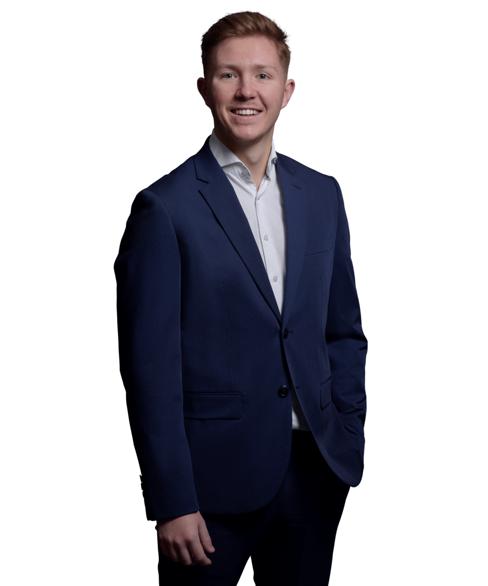 Porträtfoto von Calvin Held, Consultant bei Kemény Boehme Consultants (KBC). Junger Mann mit kurzen rotblonden Haaren und blauen Augen, lächelt freundlich in die Kamera. Trägt ein marineblaues Sakko über einem weißen Hemd.