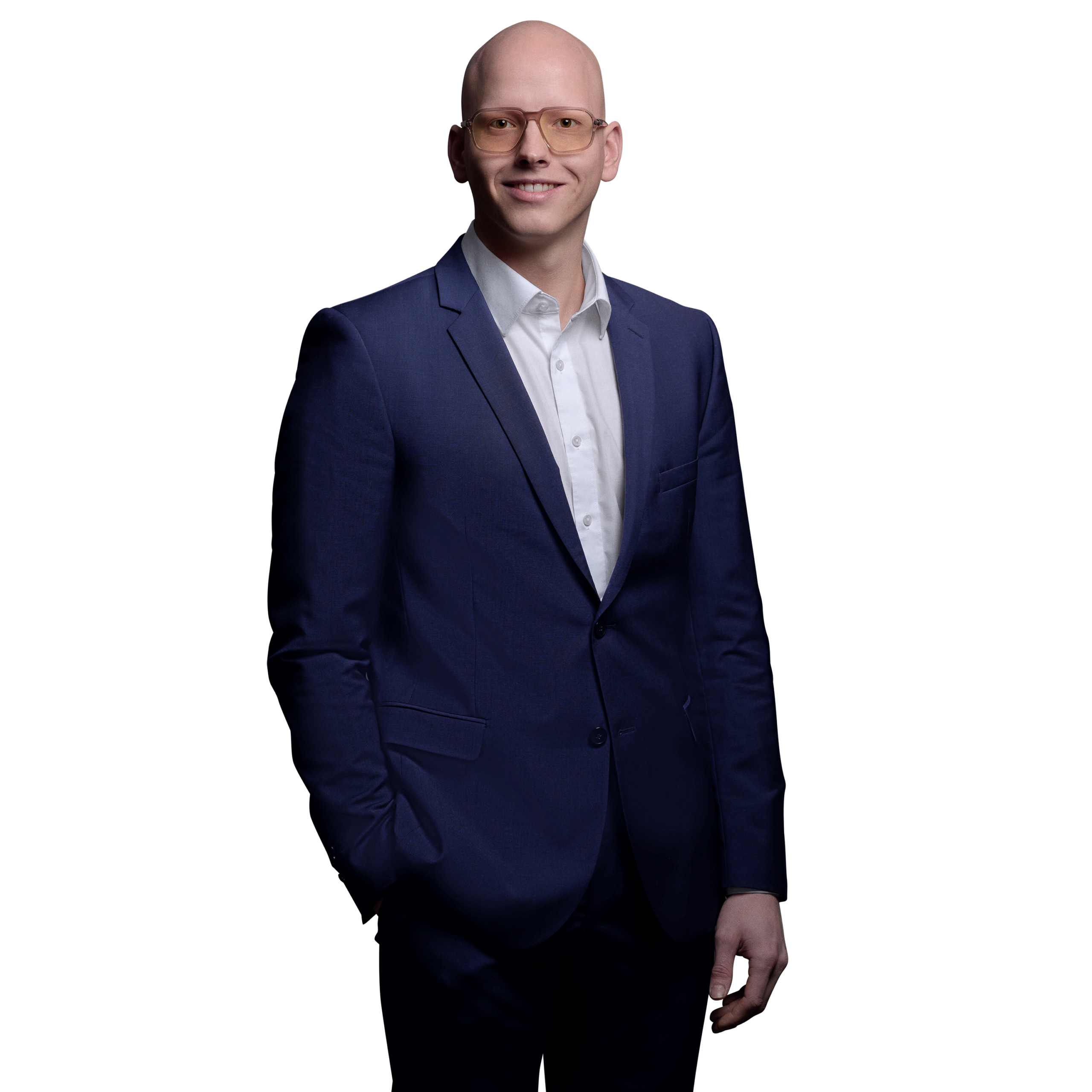 Porträtfoto von Yannic Lederer, Software Engineer bei Kemény Boehme Consultants (KBC). Mann mit rasiertem Kopf und markanter eckiger Brille mit getönten orangefarbenen Gläsern, blickt freundlich lächelnd in die Kamera. Trägt einen dunkelblauem Anzug über einem weißen Hemd ohne Krawatte, eine Hand in der Hosentasche.
