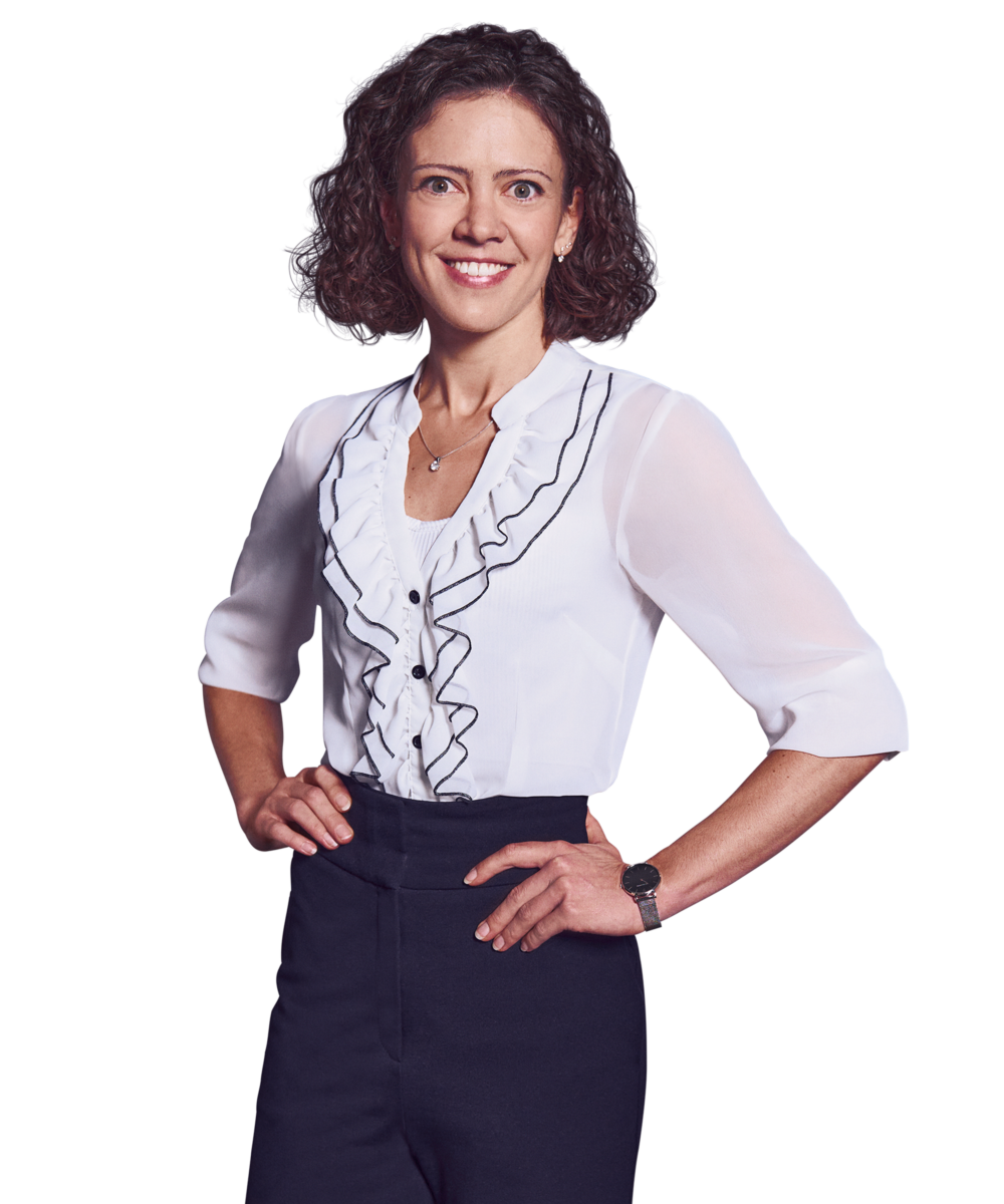 Porträtfoto von Larissa Fahrmeier, Director bei Kemény Boehme Consultants (KBC). Frau mit schulterlagen, lockigen dunkelbraunen Haaren, lächelt breit und freundlich in die Kamera. Trägt eine weiße Bluse mit Rüschendetails und schwarzen Akzenten sowie eine feine Halskette und eine silberne Armbanduhr, beide Hände an den Hüften.
