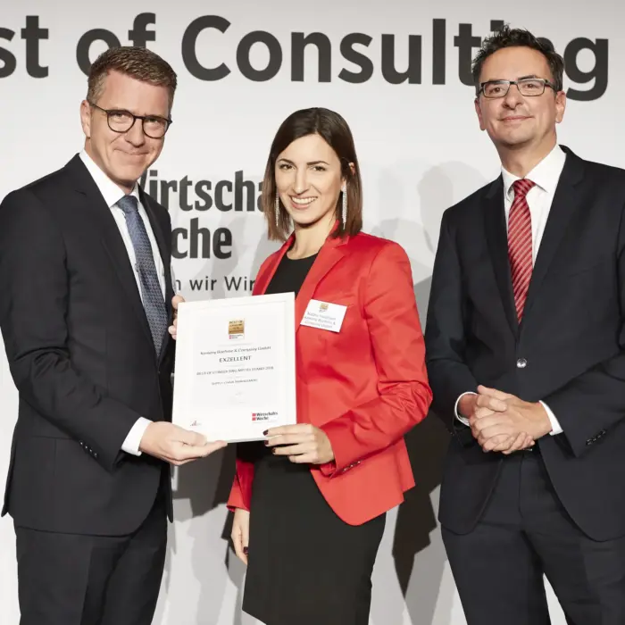 The 2018 Best of Consulting Awards ceremony, featuring Stefan Kemény on the left, along with a woman in a red blazer and a man in a black suit standing next to him.